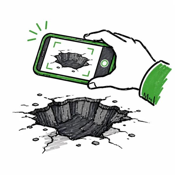 Hand holding a phone photographing a pothole in the road.